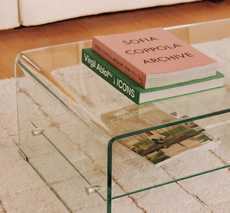 Table basse en verre avec livres de design et décoration Table basse transparente posée sur tapis beige avec livres de design et décoration, dont Sofia Coppola Archive et Virgil Abloh Icons